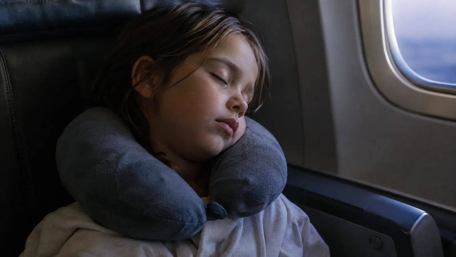 A child asleep on an airplane with a travel pillow supporting the head and chin