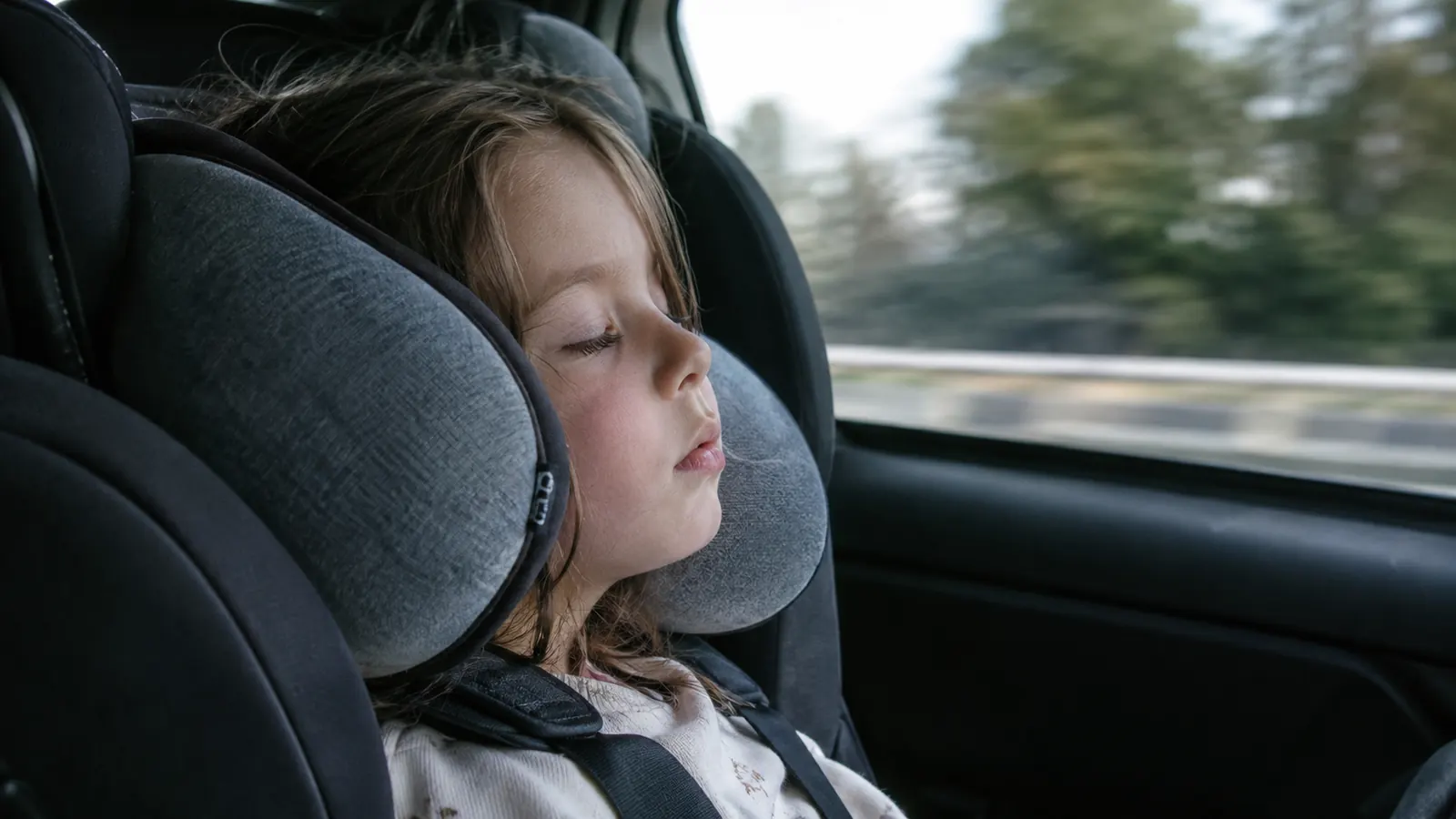 A child sleeping with head supported upright by a travel pillow while the car is moving