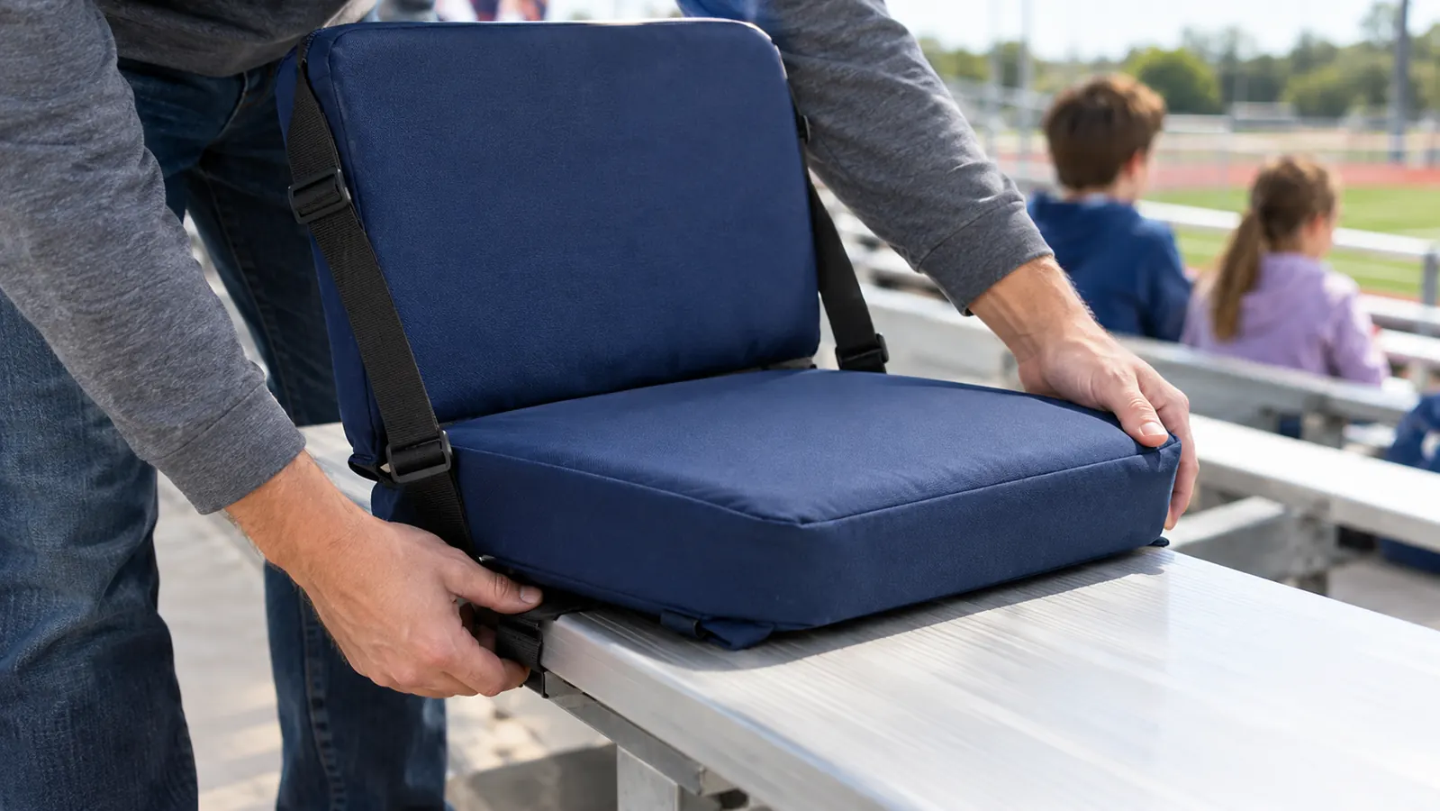 A hand clipping a padded stadium seat onto a metal bleacher bench