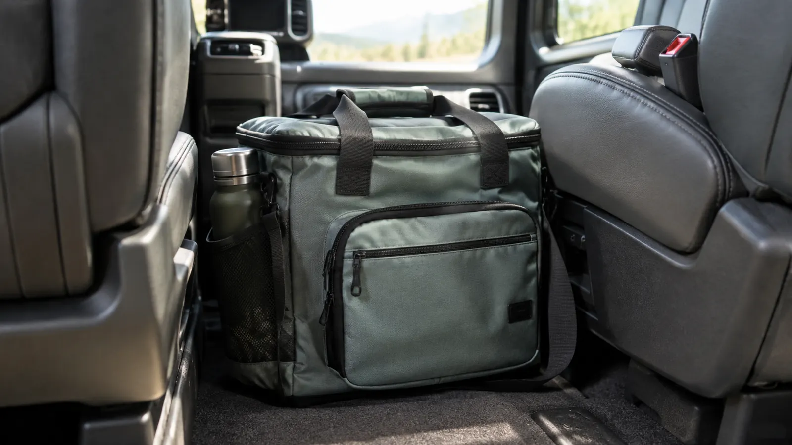 A soft-sided cooler bag on the floor of a minivan between two car seats, packed for a road trip