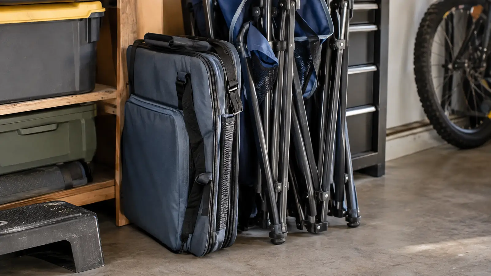 A soft-sided cooler bag folded flat and tucked upright against a stack of camping chairs in a garage