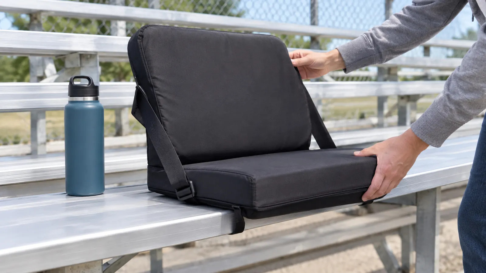 A stadium seat clipped onto a metal bleacher bench with a water bottle resting on the bench beside it