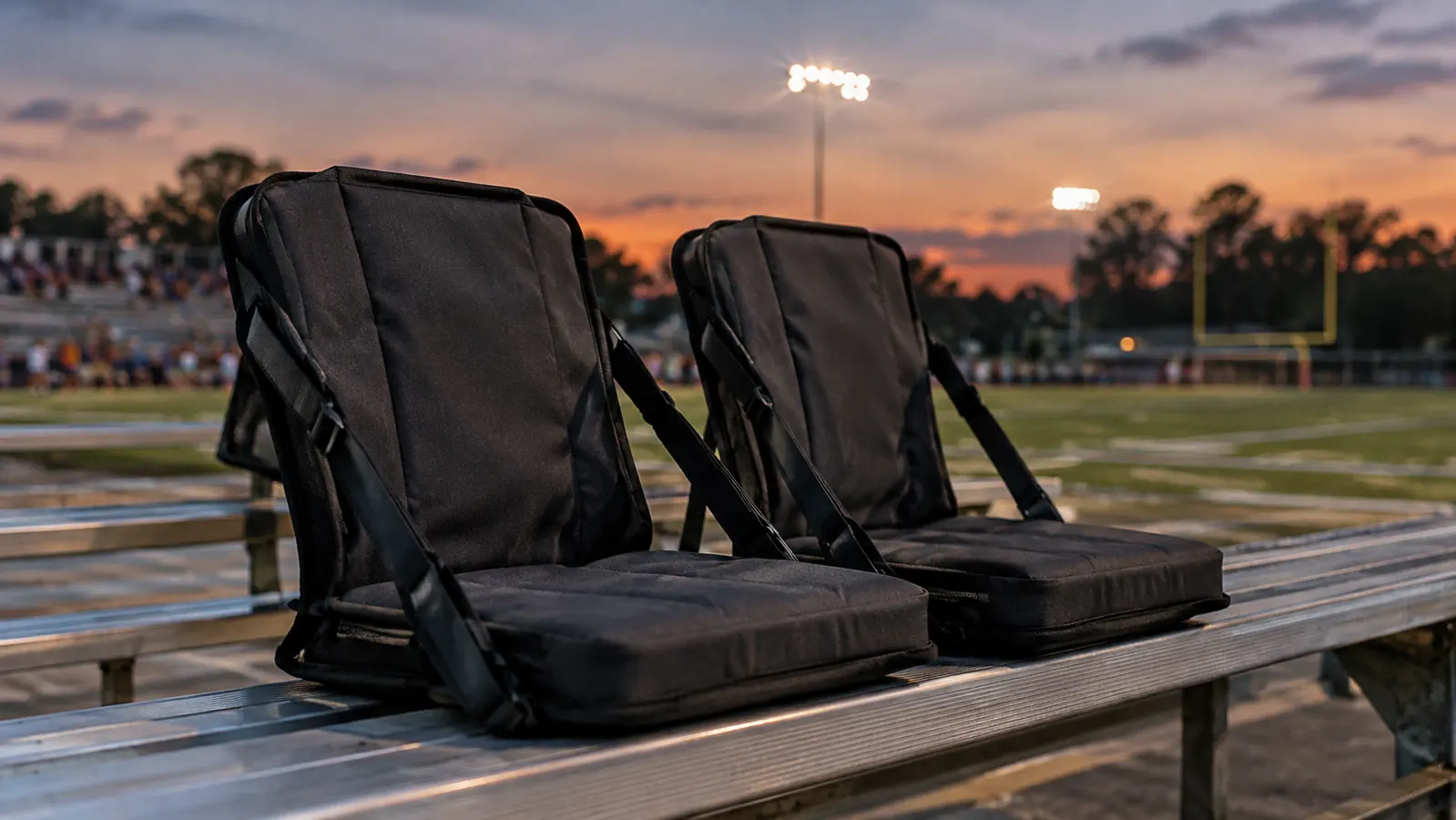 Two folded stadium seats with back support and shoulder straps resting on a bleacher bench at dusk